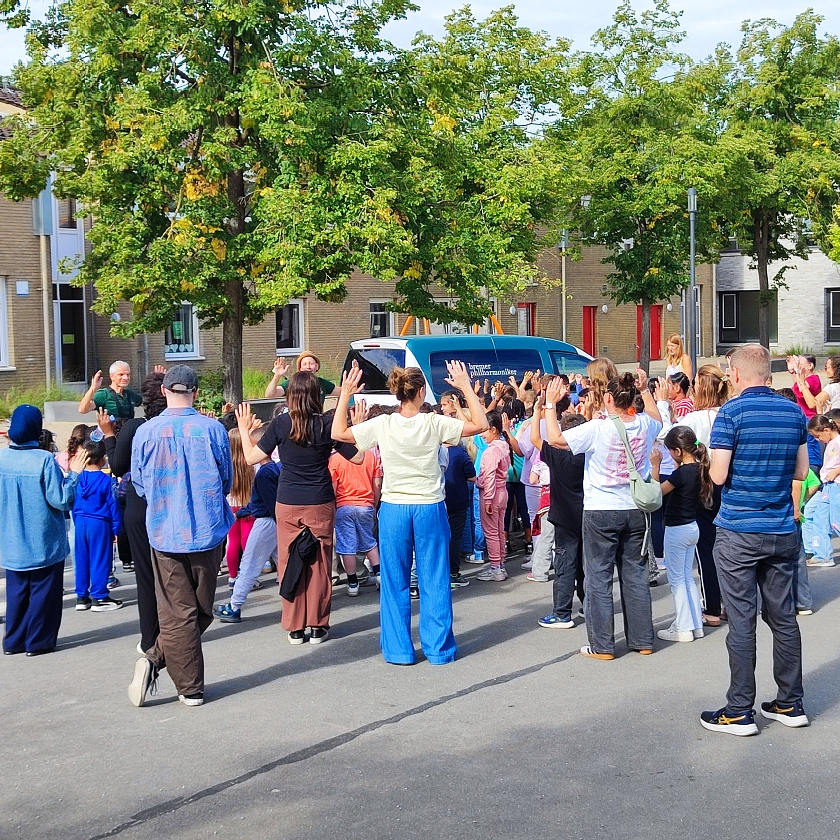 Auf dem Schulhof stehen Kinder und Erwachsene mit Rücken zur Kamera und heben die Hände