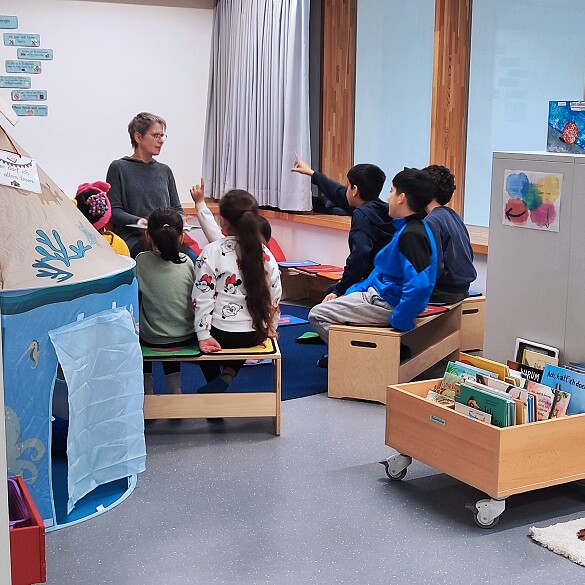 Lehrkraft bespricht mit Kindern im Halbkreis sitzend ein Buch