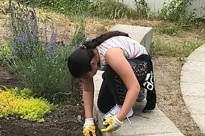 Kind sitzt in der Hocke und j&auml;tet Unkraut im Garten